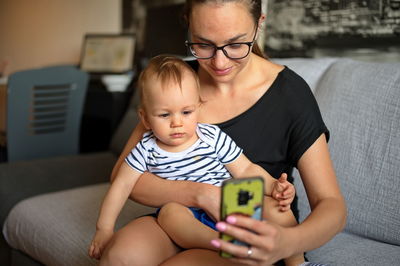 Mother and her baby boy sitting on a sofa and using mobile phone