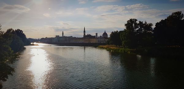 Scenic view of river by buildings against sky at sunset