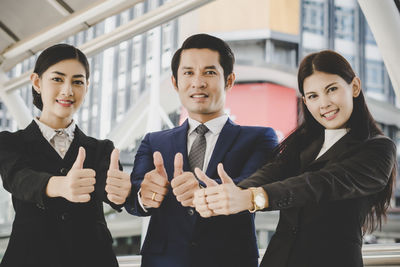 Portrait of business people showing thumbs up while standing in office corridor