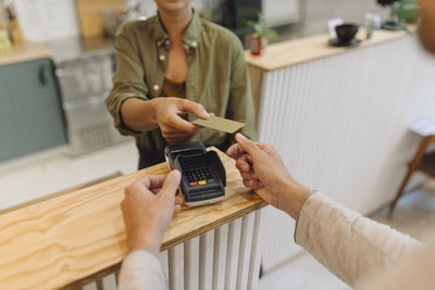 Midsection of female entrepreneur giving credit card to customer at checkout in cafe