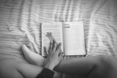 Low section of woman reading book on bed at home