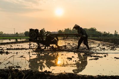 Man working at farm against sky during sunset