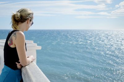 Side view of woman looking at sea while standing by railing against sky