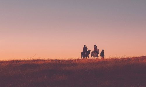 People riding on field against sky during sunset