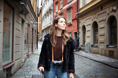 Young woman with camera looking away while standing in alley