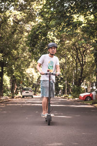 Portrait of mid adult man riding push scooter on road against trees