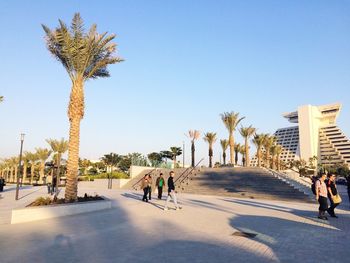 People walking against buildings against clear sky on sunny day