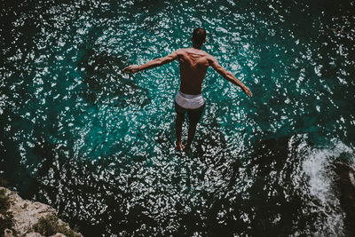 Rear view of shirtless man jumping into sea on sunny day