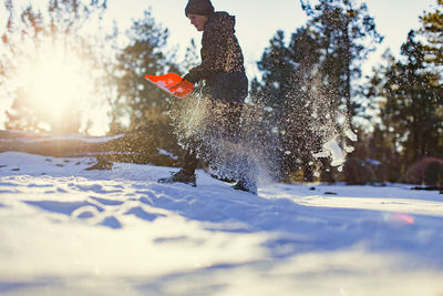 Low angle view of girl removing snow with shovel on field