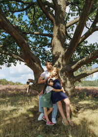 Side view of father with daughters standing under tree on field