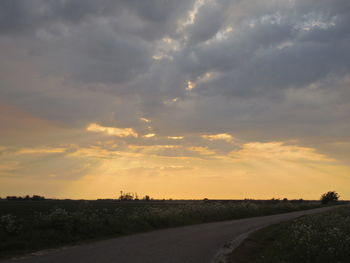 Road passing through field against cloudy sky