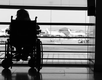 Rear view of disabled woman sitting on wheelchair against window