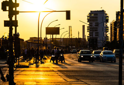 People walking on city street against sky during sunset