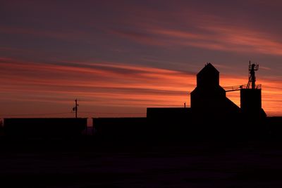 Silhouette factory against sky during sunset