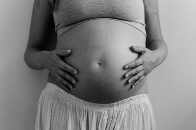 Midsection of pregnant woman standing against gray background