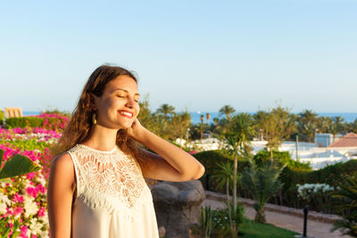 Smiling young woman with eyes closed standing against sky