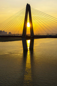 Silhouette bridge over river against sky during sunset