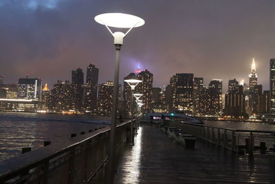 Illuminated buildings by river against sky at night