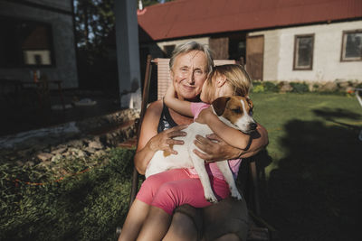 Smiling grandmother with granddaughter and dog on deckchair in garden