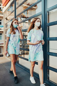 Young women girls spending time together downtown walking along store front in the city center