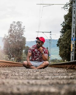 Man sitting on railroad track against sky