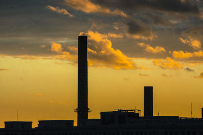 Silhouette factory against sky during sunset