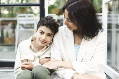 Portrait of boy sitting besides mother at back yard