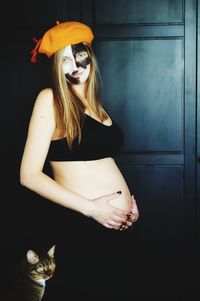 Pregnant woman with painted face standing at home during halloween