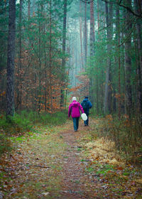 Rear view of man and woman walking on footpath amidst forest