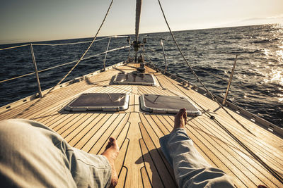 Low section of man relaxing on sailboat against sea