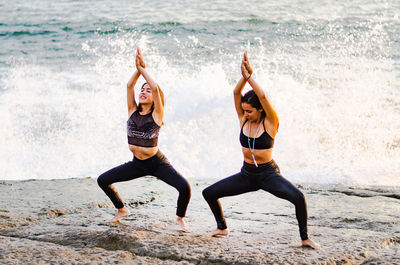 Full length of female friends doing yoga on rock at beach