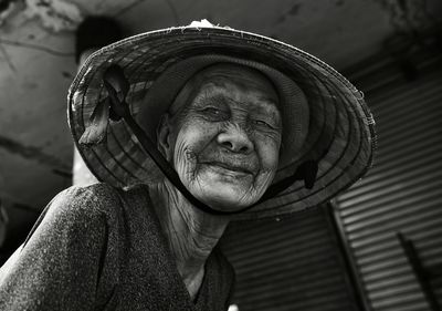 Close-up low angle portrait of smiling senior woman wearing asian style conical hat outdoors