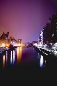 Illuminated buildings by river against clear sky at night