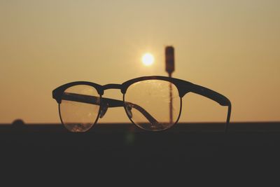 Close-up of eyeglasses against sky during sunset