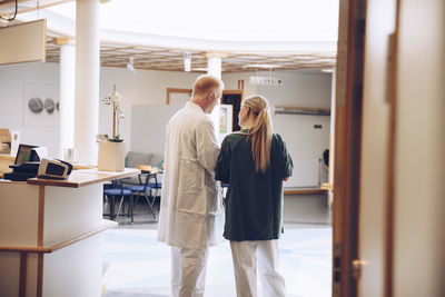 Rear view of female nurse and male doctor discussing while standing in hospital lobby