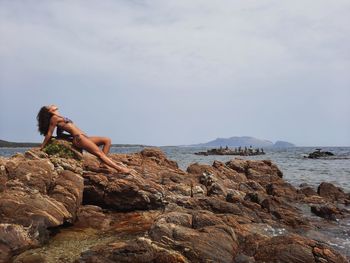 Man standing on rock by sea against sky