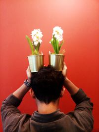 Rear view of man holding flower against red background