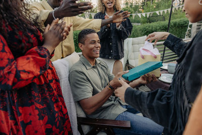 Woman giving gifts to smiling male friend during birthday celebration in back yard