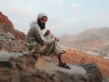 Young man sitting on rock against mountains