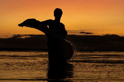 Silhouette woman in sea against sky during sunset