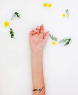 Cropped image of hand amidst flowers in milk