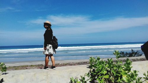 Teenage girl wearing hat while standing at beach against blue sky