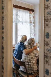 Female care assistant sitting with senior woman on chair at home