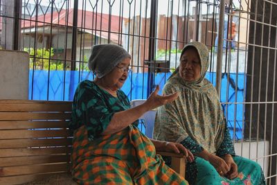 Women talking while sitting on bench against metal grate