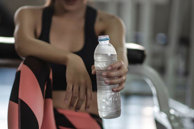 Midsection of young woman holding water bottle at gym