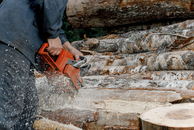 Logger, a person chopping a tree or log with a chainsaw, an electric chainsaw.