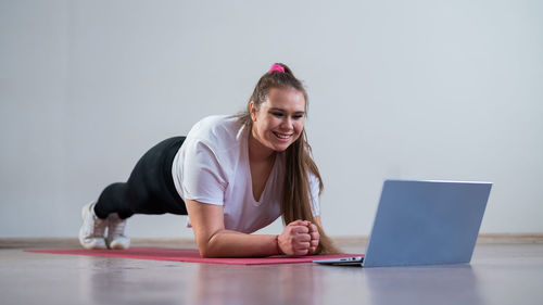 Smiling woman doing plank exercise while watching laptop