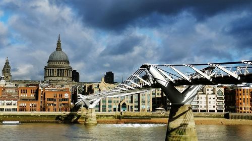 Bridge over river by buildings against sky in city
