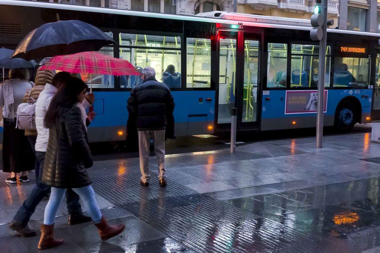 REAR VIEW OF PEOPLE WALKING ON WET ROAD