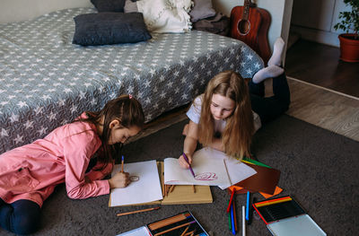 Two girls friends play at home, draw with pencils and felt-tip pens and have fun